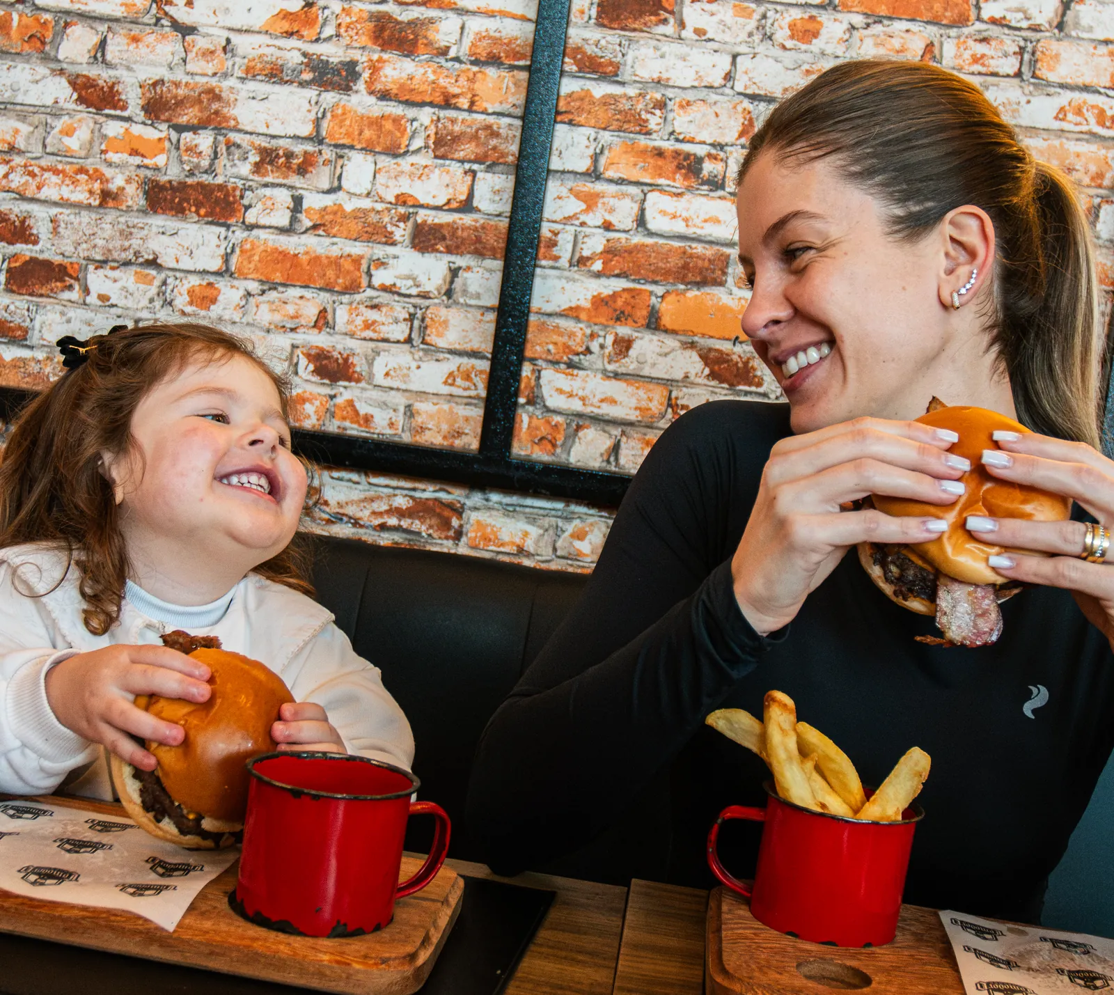 Mãe e filha rindo, cada uma com seu lanche, no salão da Comodoro